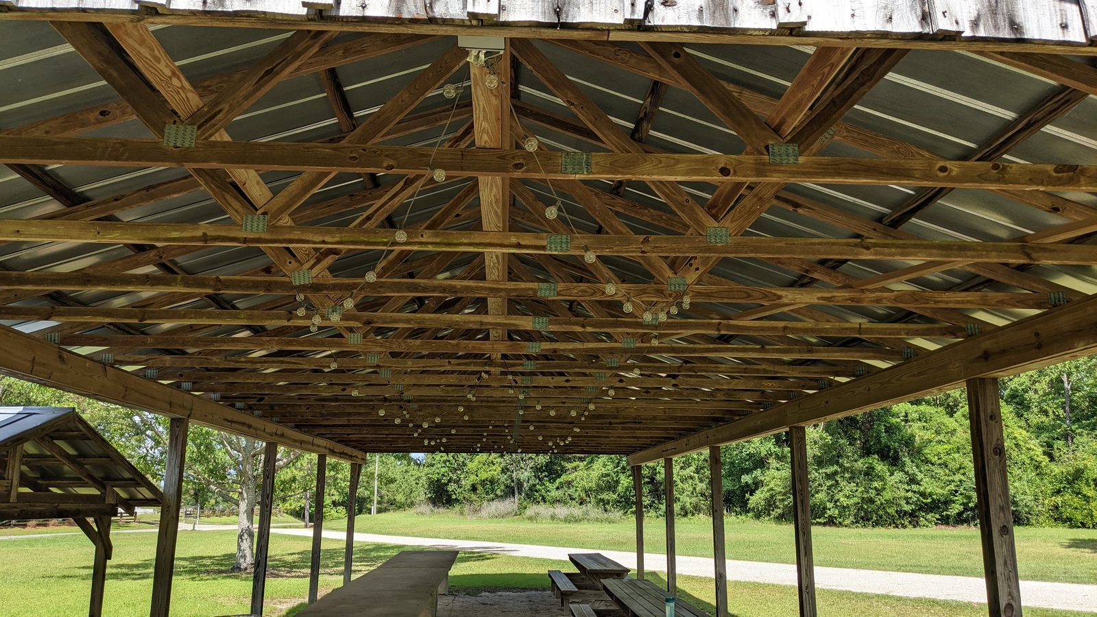 The underside of the pavilion roof before the project: exposed wooden trusses and metal decking with no light fixtures mounted.