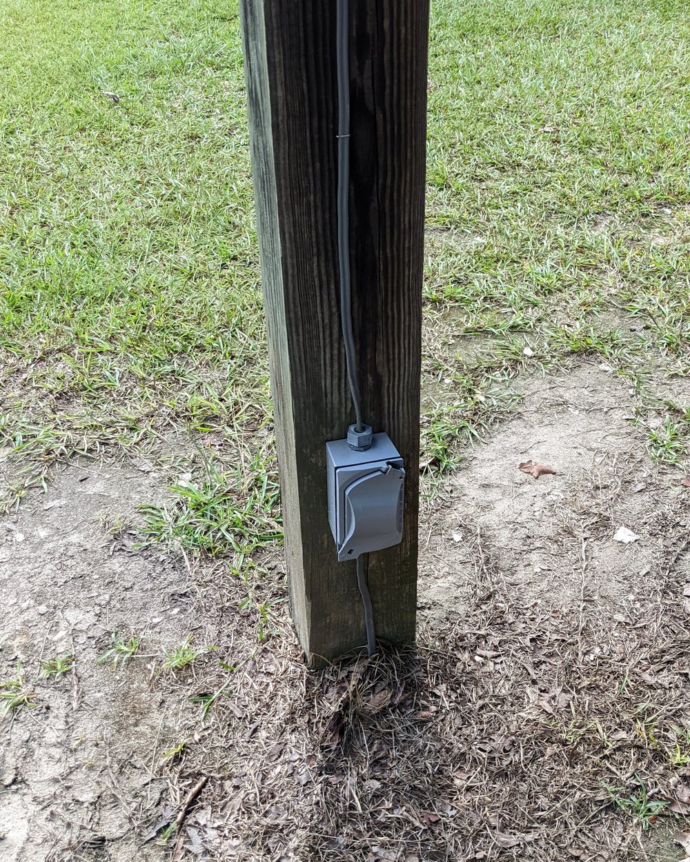 A weatherproof outlet box mounted low on a pavilion post, with cable running down the post and into the ground.